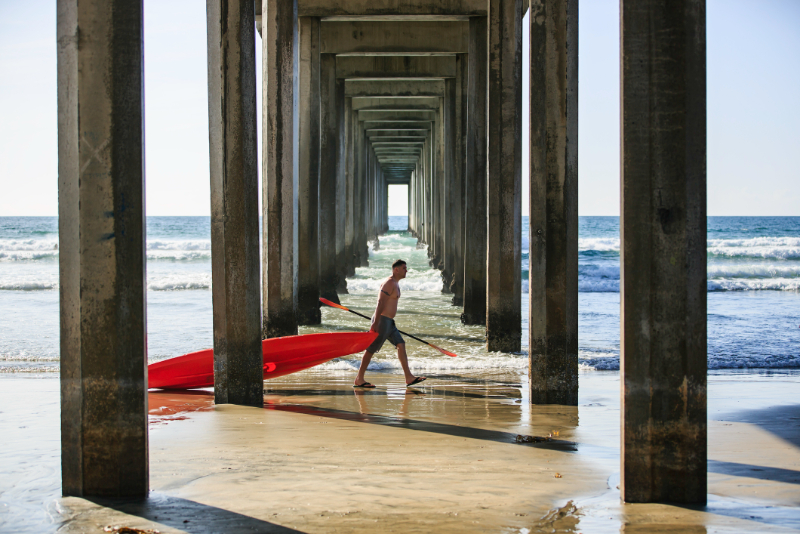 man carrying surfing board at La Jolla Shores